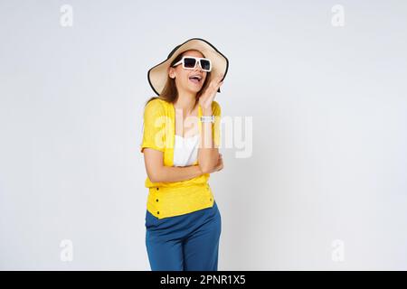 Junge Frau mit Sonnenhut und Sonnenbrille mit offenem Mund, die die Hände hebt, schreiende Ankündigung isoliert auf weißem Hintergrund. Stockfoto