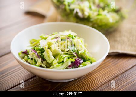 Junger Kohlsalat mit violetten Zwiebeln in einer Schüssel auf einem Holztisch. Stockfoto