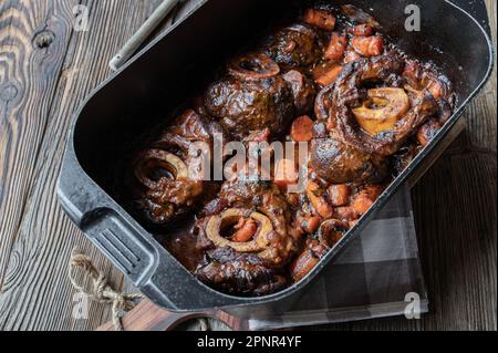 Geschmorte Rinderschäfte oder Ossubuco in einem Rösttopf auf einem Holztisch. Stockfoto