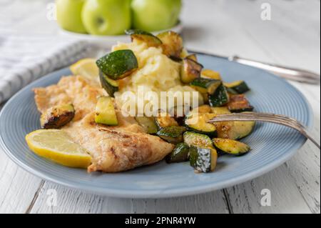 Gebratenes Fischfilet in der Pfanne mit Kartoffelpüree und gerösteter Zucchini auf einem Teller Stockfoto