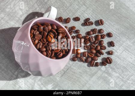 Kaffeebohnen in der Tasse auf dem Tisch und Kaffeebohnen um die Tasse Stockfoto