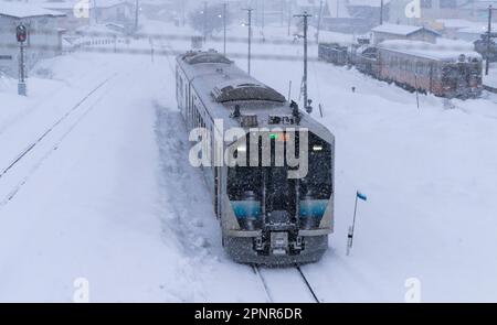 Ein Zug der JR East GV-E400-Serie, der an einem verschneiten Tag am Bahnhof Goshogawara in der Präfektur Aomori, Japan, eintrifft. Stockfoto