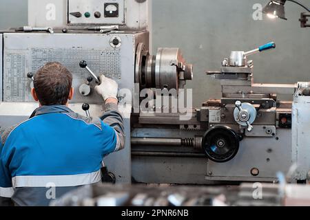 Turner an der Drehmaschine am Arbeitsplatz. Blick auf den Arbeiter von hinten. Metallverarbeitung in der Drehwerkstatt. Geräteeinstellung.. Stockfoto