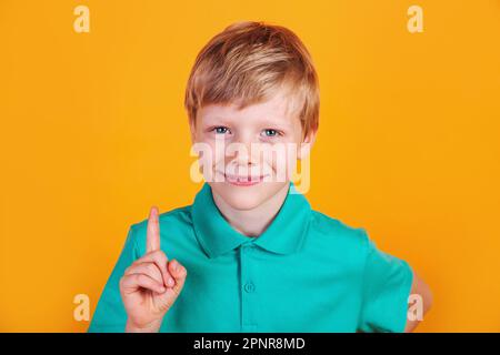 Kleiner lächelnder Junge in lässiger Kleidung, der auf den Kopierraum mit Vorfuss auf gelbem Hintergrund zeigt Stockfoto