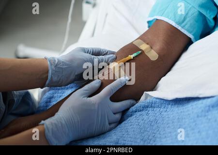 Nahaufnahme einer Krankenschwester, die den Katheter in den Arm des Patienten einführt, während er auf der Station auf dem Bett liegt Stockfoto