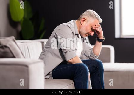 Attraktiver Mann, der sich verzweifelt traurig fühlt, besorgt aussieht, depressiv, aufmerksam und einsam leidet, Depressionen auf der Couch zu Hause Stockfoto