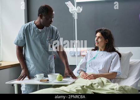 Afroamerikanischer Krankenpfleger serviert Mittagessen für jungen Patienten auf der Krankenhausstation Stockfoto