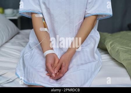 Nahaufnahme einer jungen Patientin mit Katheter im Arm, die auf dem Bett in der Station sitzt Stockfoto