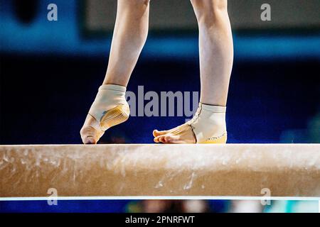Nahaufnahme Beine weibliche Turnerin tritt in Gymnastik auf Balancestrahl, passgenaue Neopren-Knöchelstütze mit Fersenschale Stockfoto
