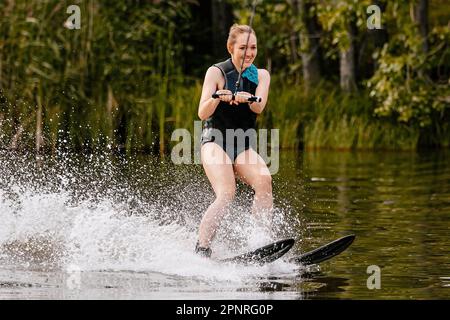 Wunderschöne junge Frau, die hinter einem Motorboot auf dem See Wasserski fährt, extreme Wassersportarten, Sommerurlaub Stockfoto