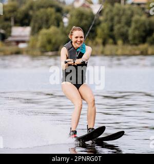 Lächelnde Frau, Wasserski hinter dem Motorboot auf dem Teich, extremer Wassersport, Sommerurlaub Stockfoto