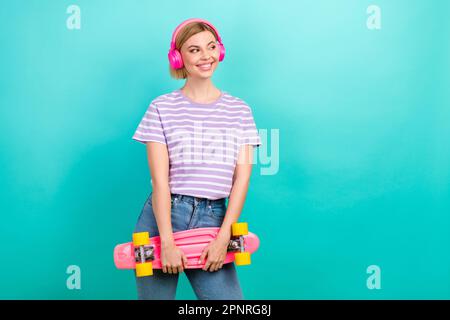 Fotowerbung mit Hipster Girl Genießen Sie ihren kabellosen Apfel airpods Pro Hold Longboard Look isoliert auf cyanfarbenem Hintergrund Stockfoto