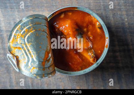 Dose Sprotten in Tomatensauce Öffnen auf einer hölzernen Hintergrund, Nahaufnahme, Ansicht von oben Stockfoto