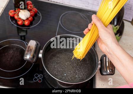 Die Hand des Kochs lässt die Spaghetti in einen Topf mit kochendem Wasser fallen Stockfoto