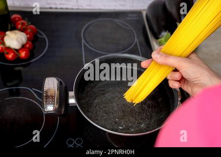 Die Hand des Kochs lässt die Spaghetti in einen Topf mit kochendem Wasser fallen Stockfoto