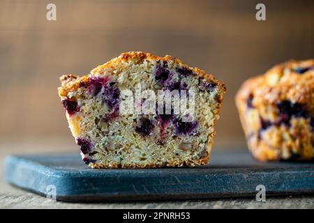 Halber Muffin mit Blaubeeren und Walnüssen auf einem Holztisch, Nahaufnahme. Süßes Gebäck auf dem Brett. Frische Cupcakes zum Frühstück Stockfoto