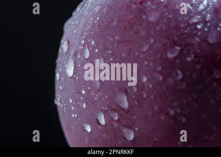 Roter Apfel mit Wassertropfen, Makroaufnahme. Der rohe Apfel auf schwarzem Hintergrund, Nahaufnahme, selektiver Fokus Stockfoto