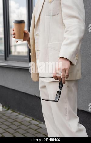 Zugeschnittener Blick auf einen schwulen Mann im Anzug, der eine Sonnenbrille und Kaffee hält, um nach draußen zu gehen, Stockbild Stockfoto