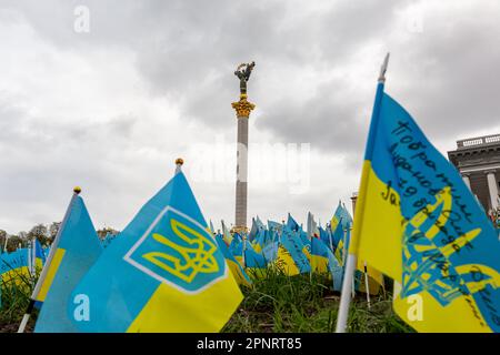 Blaue und gelbe ukrainische Nationalflaggen mit Namen gefallener Soldaten sind vor der Unabhängigkeitsstatue auf dem Maidan Nezalezhnosti (Unabhängigkeitsplatz) im Zentrum Kiews, der Hauptstadt der Ukraine, zu sehen. Familien und Freunde der getöteten Soldaten hinterlassen Flaggen als Gedenkstätte für ihre Angehörigen, da die Invasion der Ukraine durch die russischen Streitkräfte in vollem Umfang anhält. Stockfoto