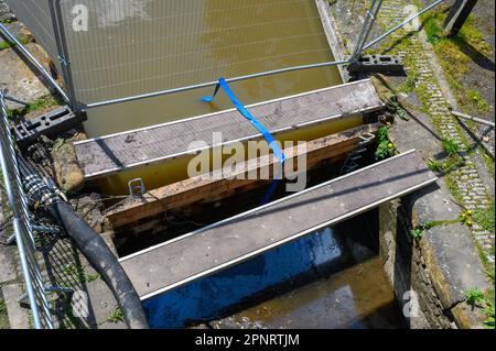 Von einer Brücke nach unten schauen, um die Bretter daran zu hindern, einen Damm zu errichten, um zu verhindern, dass Wasser entlang eines Kanals fließt, der gerade gebaut wird. Stockfoto