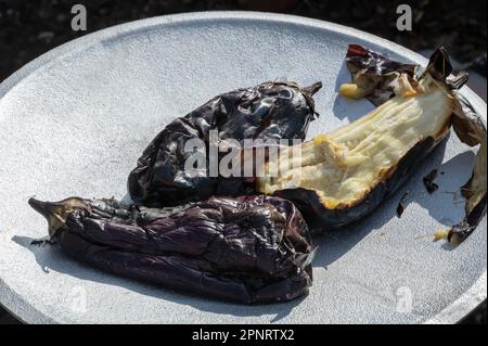 Gesundes vegetarisches Gericht mit gegrillter Aubergine. Ganze Auberginen werden auf einem offenen Herdfeuer gekocht. Fertig zubereitete Beilage für ein Fleischgericht. Stockfoto