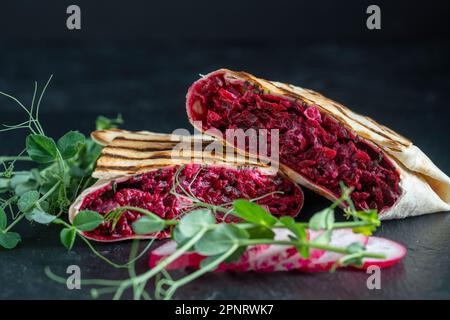 Veganer Burrito. Aufgeschnittene rohe Lebensmittelverpackung mit roter Rote Beete, Feta-Käse, Pflaumen, Dill und Rahmsoße mit Erbsen-Mikrogemüse auf einem Teller. Nahaufnahme Stockfoto