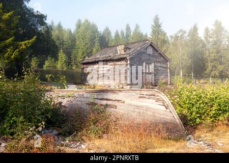 Alte Holzlager, Scheunen und Schuppen am Ufer. Nebeliger Morgen am Meer. Ein Holzboot auf dieser Seite. Stockfoto