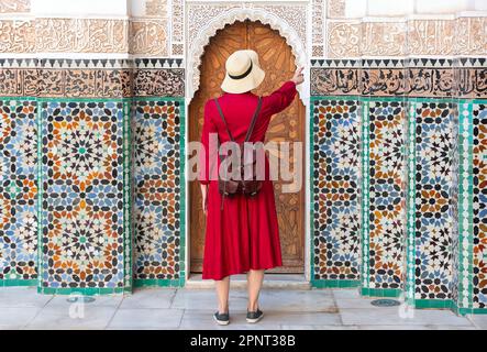 Ein Mädchen in Rot mit Hut, das auf den Ben Youssef Madrasa in marrakesch, marokko, schaut Stockfoto