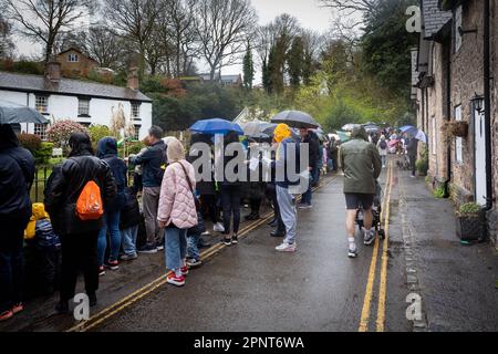 Überfüllte Dorfstraße im Regen und unter Sonnenschirmen, die an der Ziellinie des Lymm Duck Race 2023 warten Stockfoto