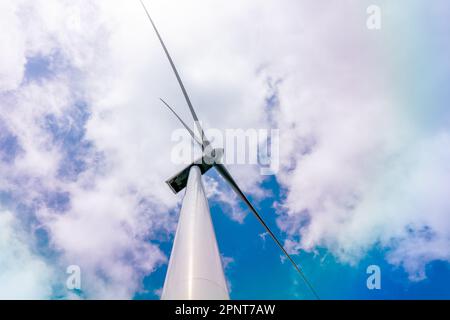 Ansicht von unten auf eine Windturbine, die Elektrizität erzeugt saubere Energie mit Wolken- und Sonnenlicht-Hintergrund am Himmel. Konzept für saubere Energie. Hochwertiges Fotopapier Stockfoto