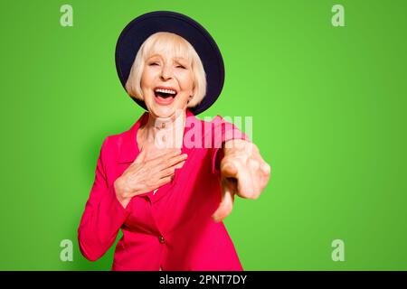 Du bist eine Witzfigur, Großmutter, die mit Zeigefinger auf die Kamera zeigt und laut lacht, isoliert auf lebendigem gelbem Hintergrund Stockfoto