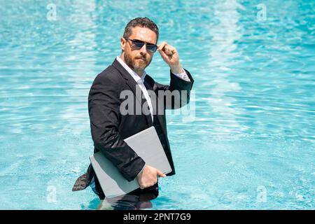 Lustiger Freiberufler, Fernarbeit, E-Arbeit. Sommer-Witzfigur. Geschäftsmann im Anzug, der an einem Laptop im Wasserpool arbeitet. Geschäftsmann will Stockfoto