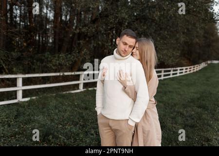 Ein junges, glückliches, romantisches schwangeres Paar geht an warmen Herbsttagen mit Händchen nach draußen. Schwangere Frau in Strickkleid und ihr gutaussehender Mann erwarten Stockfoto