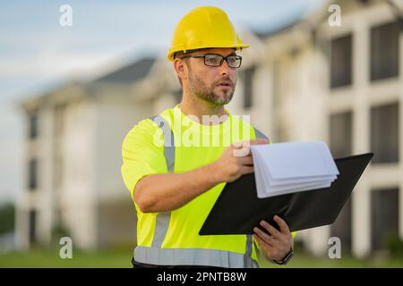 Bauarbeiter vor Ort. Arbeiter mit Schutzhelm. Bauarbeiter im Helm beim Bau eines neuen Wohngebäudes. Ingenieur mit Zwischenablage Stockfoto