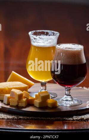 Gläser belgisches gelbes, blondes und dunkelbraunes Bier, hergestellt in Abbey und Holzbrett mit einer Vielzahl belgischer Käsesorten, Speisen und Bier in Belgien Stockfoto