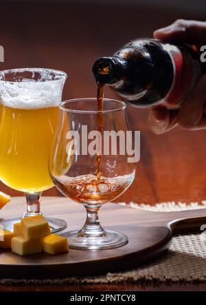 Gläser belgisches gelbes, blondes und dunkelbraunes Bier, hergestellt in Abbey und Holzbrett mit einer Vielzahl belgischer Käsesorten, Speisen und Bier in Belgien Stockfoto