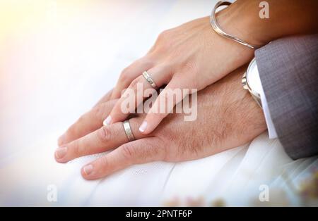 Die Hände von Braut und Bräutigam überlappen sich und zeigen die Eheringe auf dem Brautkleid. Stockfoto