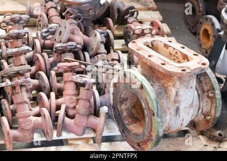 Große rostige alte Metallschieber, Rohrfittings, vor dem Hintergrund von kleinen Ventilen, Rohrleitungsventile in der Fabrik, Werkstatt. Konzeptindustrie, Arbeit Stockfoto