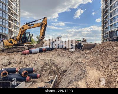 Gelber Hydraulikbagger hat ein tiefes Loch in den Boden gegraben. Kommunikation für Wohngebäude. Verlegen von Gummischläuchen für Wasser und Rohrleitungen. Stockfoto