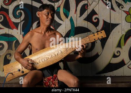 Kuching, Sarawak - 13. Mai 2022: Traditioneller Tänzer im Sarawak Village, demonstrieren Sie seine traditionelle Gitarre namens sape Stockfoto