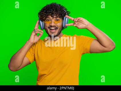 Ein glücklicher inder mit Kopfhörern hört Musik und tanzt in der Disco herum, hat lustige, ausdrucksstarke, gestikulierende Hände, entspannt auf einer Party. Hindu-Typ isoliert, allein auf Studio Chroma Key Hintergrund Stockfoto