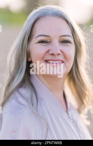 Eine wunderschöne, grauhaarige ältere Frau auf der Straße sieht in die Kamera und lächelt. Das Konzept eines glücklichen und schönen Alters Stockfoto