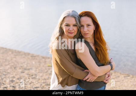 Grauhaarige ältere Frau Mutter mit erwachsener Tochter umarmt am Strand an einem sonnigen Tag, Generationsbeziehung, Nahaufnahme Stockfoto