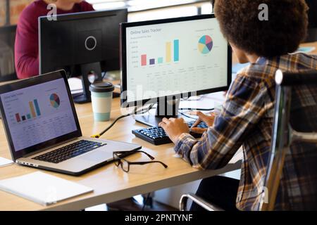 Vielbeschäftigte, birassistische, legere Geschäftsfrau, die am Schreibtisch mit einem Kollegen im Büro an einem Computer und Laptop arbeitet Stockfoto