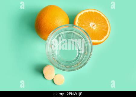 Glas Wasser, Vitamin-C-Brausetabletten und Orangen auf türkisfarbenem Hintergrund Stockfoto