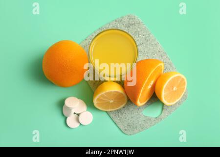 Brett mit einem Glas Vitamin-C-Brausetablette, gelöst in Wasser und Früchten auf türkisfarbenem Hintergrund Stockfoto