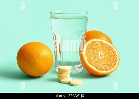 Glas Wasser, Vitamin-C-Brausetabletten und Orangen auf türkisfarbenem Hintergrund Stockfoto