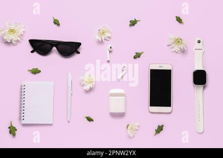 Komposition mit modernen Geräten, Notizbuch, Sonnenbrille und Blumen auf farbigem Hintergrund Stockfoto