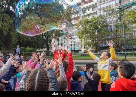 Lucas Acosta, der unter dem Namen Toto auftritt, stellt am 20. Juli 2022 in einem Park in Buenos Aires, Argentinien, eine große Seifenblase für ein Publikum von Kindern her. Acosta nutzt die Winterschulferien, um seine Dienste für Kinderpartys anzubieten und zu bewerben. „Die Straße hat etwas, das für einen Künstler immer ein Segen ist“, sagt er. „Sie können jederzeit auftauchen, und die Leute sind immer verfügbar.“ (Lucila Pellettieri/Global Press Journal) Stockfoto