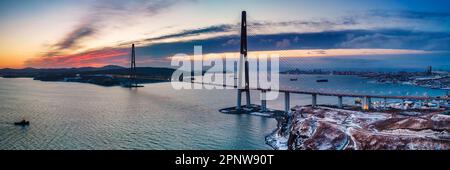 Winterpanorama-Blick auf den Sonnenuntergang über der berühmten Kabelbrücke von Wladiwostok zur Insel Russky, weit östlich von Russland Stockfoto